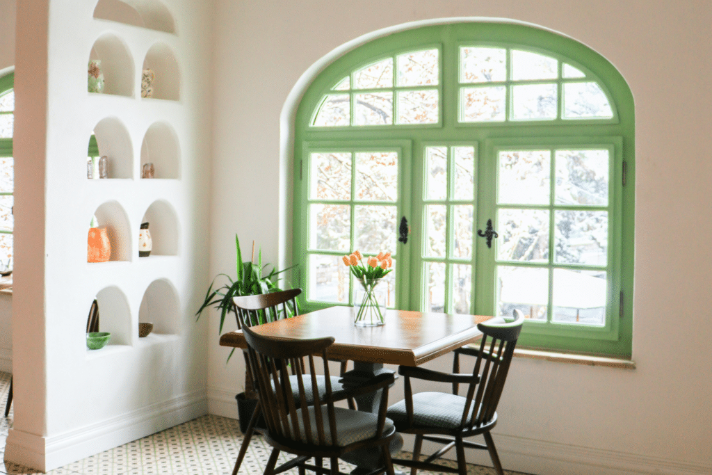 New windows that don't cost so much. They are green and behind a kitchen table with flowers on it.